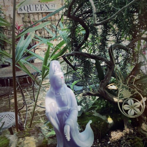 Photo of Jenelle’s Garden. In the garden is a statue of Quan Yen and a street sign that reads “Queen Street.”